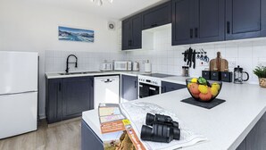 Una cocina moderna con armarios oscuros, encimeras blancas y diversos electrodomésticos, como lavavajillas, microondas y cocina.