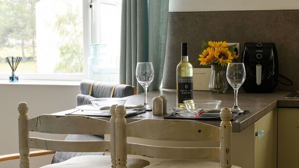 Un coin repas avec une table dressée pour deux personnes, une bouteille de vin et une machine à café.