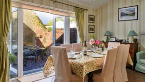 A dining area with a table set for four, a chandelier, and a view of the garden through a sliding glass door. - Stunning  villa for 10 people with WIFI and pets allowed (Portmadoc)