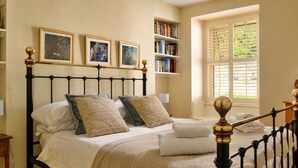 A neatly arranged bedroom with a bed, bedside tables, a bookshelf, and a window with blinds. - Stunning  villa for 10 people with WIFI and pets allowed (Portmadoc)