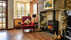 A cozy living room with a stone fireplace, a red armchair, and a television. - Stunning  villa for 10 people with WIFI and pets allowed (Portmadoc)