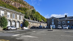 A street with stone buildings, parked cars, and a clear blue sky. - Stunning  villa for 10 people with WIFI and pets allowed (Portmadoc)