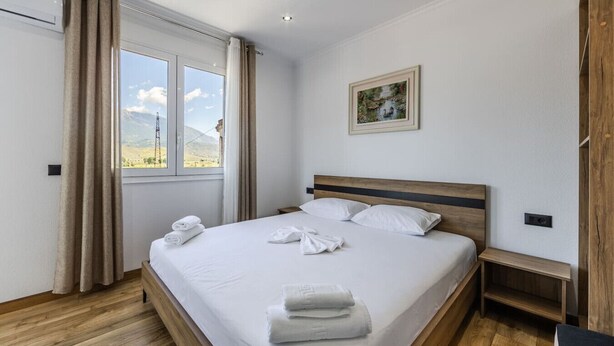 A hotel room with a large bed, a wooden headboard, a bedside table, and a window with curtains.