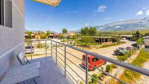 A balcony with a view of a parking area, a red vehicle, and distant mountains.