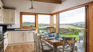 A kitchen with a dining area, large windows, and a view of the countryside. - Stunning  villa for 8 guests with WIFI, TV and balcony (Aberdaron)