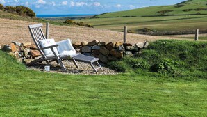 A chair with a towel and a stone wall in a grassy field with a view of the sea. - Stunning  villa for 8 guests with WIFI, TV and balcony (Aberdaron)