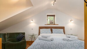 Une chambre à coucher avec un grand lit, un fauteuil vert et une petite table avec une lampe.