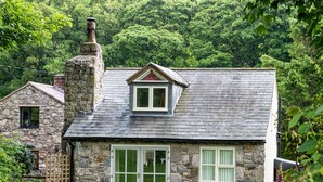 Une maison en pierre avec un toit en pente, une cheminée et une petite fenêtre de grenier.