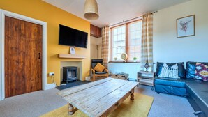 Una sala de estar acogedora con una mesa de madera, un televisor montado en la pared, una chimenea y un sofá con cojines.