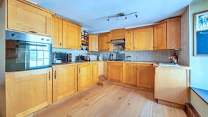 Una cocina con armarios de madera, horno empotrado, microondas y hervidor.