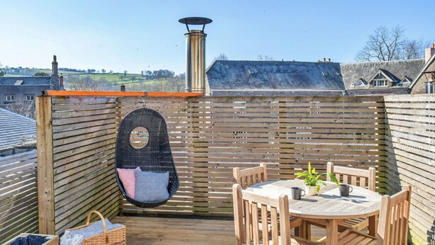Una terraza de madera con una mesa redonda y sillas, una silla colgante y una chimenea.