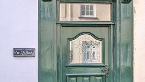 Una puerta verde con un ventanal pequeño y un letrero en la pared que dice 'Yr Daflod'.