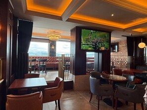 A restaurant with a terrace, tables, chairs, a TV screen, and a view of the sea. - Bayview Lodge (Downings)