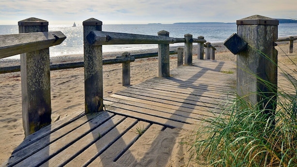 Un passeig de fusta que condueix a una platja amb una vista clara de l'oceà i muntanyes llunyanes.