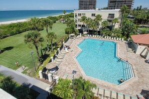 A swimming pool surrounded by lounge chairs and umbrellas, with a view of the beach and ocean.