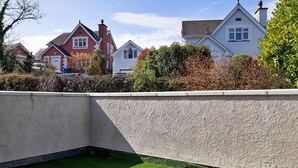 Un jardí paisatjistic amb un mur de contenció de formigó, gespa verda i cases al fons.