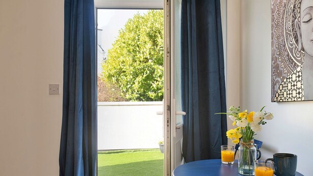 Una habitació amb una porta que dona a un balcó, una taula petita amb begudes i un vas amb flors.
