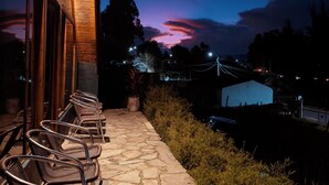Un espace extérieur aménagé avec un sol en pierre, des chaises en osier, un bâtiment en bois doté de grandes fenêtres et une vue sur le ciel au crépuscule.