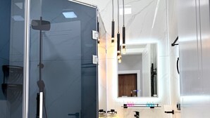 A modern bathroom with a glass-enclosed shower, a vanity with a mirror, and a sink.
