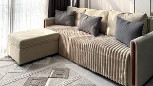 A modern living room with a sofa, ottoman, and a large window with curtains.