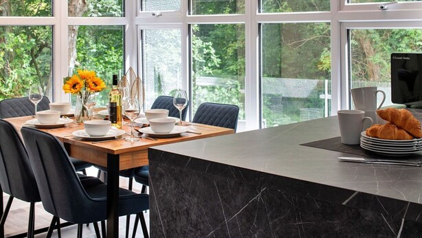A modern dining area with a large window, a marble island, and black chairs. - Stunning  villa for 5 guests with WIFI and pets allowed (Llangelynin)
