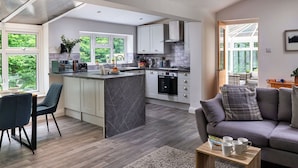 A modern kitchen with a central island, white cabinetry, and a dining area with a dark blue chair. - Stunning  villa for 5 guests with WIFI and pets allowed (Llangelynin)
