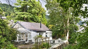 A stone house with a glass conservatory, surrounded by lush greenery and a stone wall. - Stunning  villa for 5 guests with WIFI and pets allowed (Llangelynin)