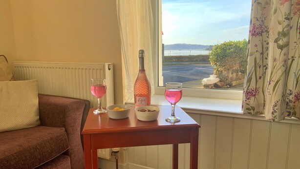 Ein gemütliches Wohnzimmer mit einem braunen Sofa, einem Holztisch mit zwei Gläsern rosa Getränken, einer Flasche und Schalen mit Snacks.
