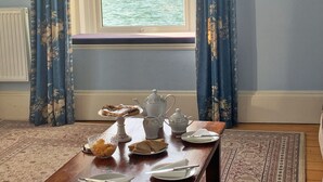 A dining table with a view of a body of water through a window, curtains, and a rug.
