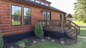 Una cabaña de troncos con terraza, ventanas amplias y un pequeño jardín.