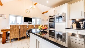 Una cocina moderna con armarios blancos, encimera negra y electrodomésticos de acero inoxidable. Hay una zona de comedor con una mesa y sillas estampadas.