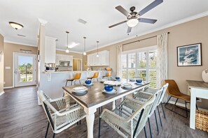 A dining area with a large table, wicker chairs, ceiling fans, pendant lights, and a view through the window.