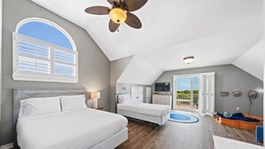 A bedroom with two beds, a ceiling fan, a TV, and a balcony with a view. - Spacious Family-Friendly | Pet-Friendly Beach House | Pool | Sleeps 10 (Gulf Shores)