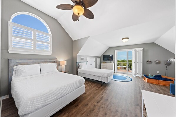 A bedroom with two beds, a ceiling fan, a TV, and a balcony with a view. - Spacious Family-Friendly | Pet-Friendly Beach House | Pool | Sleeps 10 (Gulf Shores)