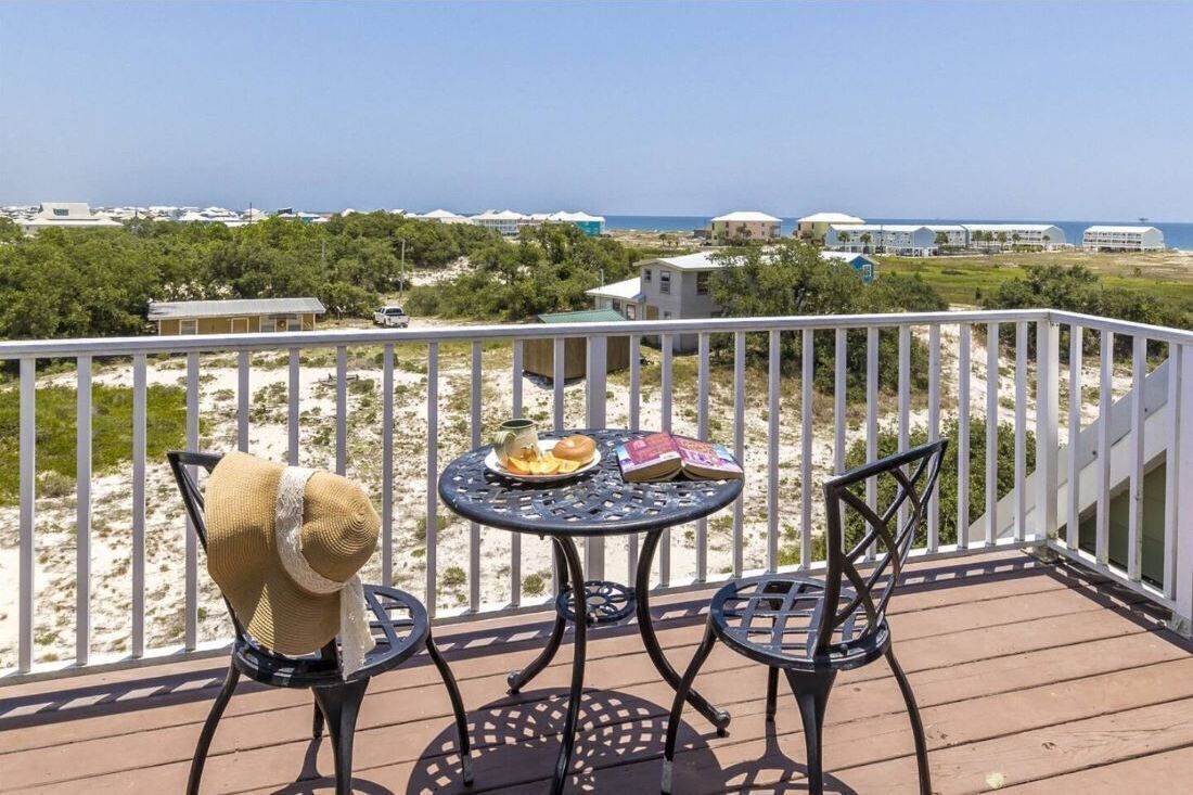Een balkon met een tafel en stoelen, met uitzicht op een strand en de oceaan.