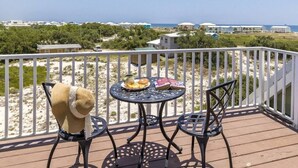 A balcony with a table and chairs, overlooking a beach and ocean. - Spacious Family-Friendly | Pet-Friendly Beach House | Pool | Sleeps 10 (Gulf Shores)