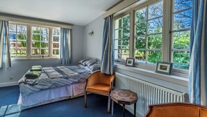 A bedroom with a bed, a chair, a small table, and large windows with curtains.