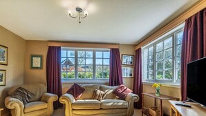 A cozy living room with a sofa, armchairs, a TV, and a window with curtains.