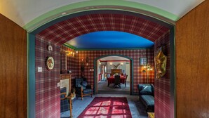 A room with a red plaid wallpaper, a blue ceiling, a fireplace, a dining area, and a hallway leading to another room.