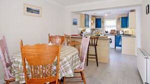 A compact kitchen with blue cabinets, a central island, and a dining area with wooden chairs and a table.