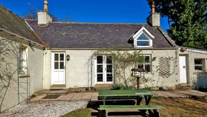 A stone house with a tiled roof, a wooden bench, and a gravel pathway.