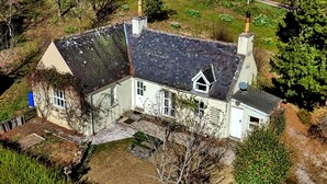 A large, single-story house with a sloped roof, a chimney, and a small garden area.