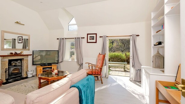 A spacious living room with a fireplace, television, and comfortable seating. A large window offers a view of the garden.