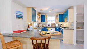 A modern kitchen with blue cabinets, a central island, and a dining area with a wooden chair.