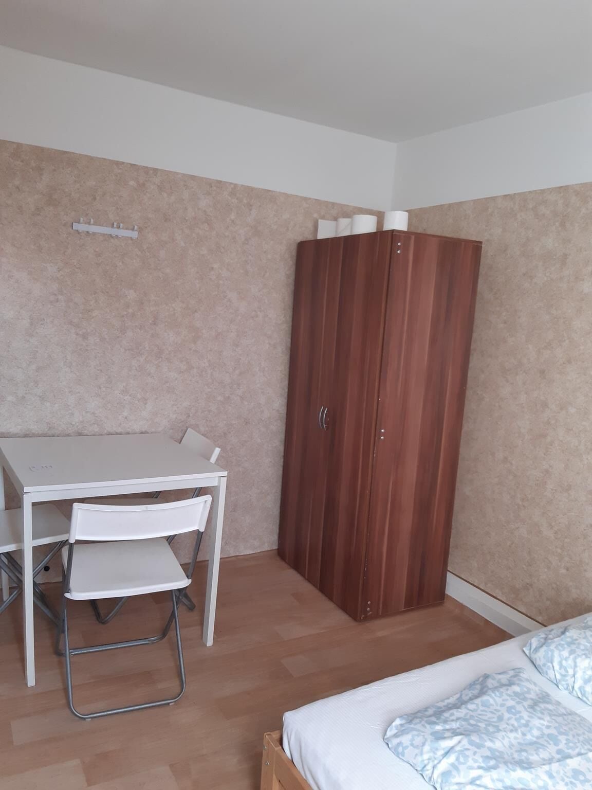 Una habitación pequeña y ordenada con un escritorio blanco, una silla, un armario y una cama.