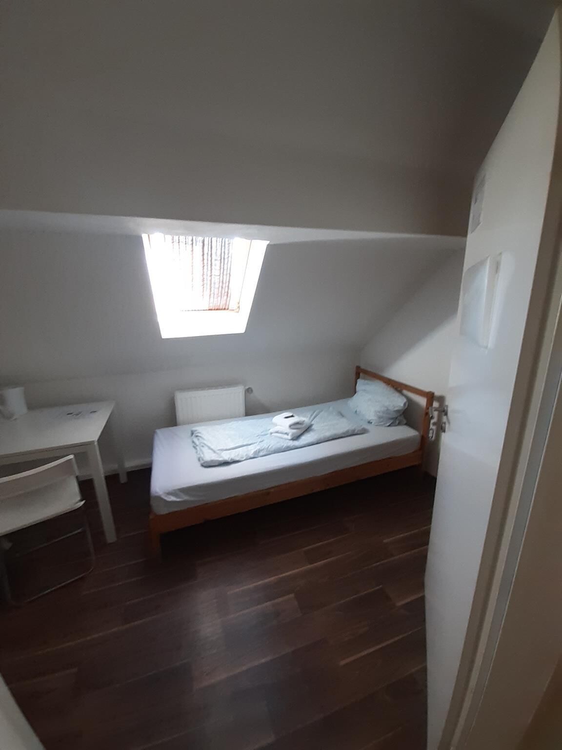 Una habitación pequeña con cama individual, techo inclinado y tragaluz.