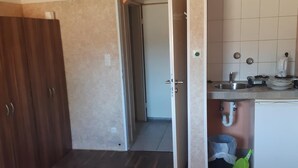 A compact room with a bed, a small table, a kitchenette with a sink and stove, and a door leading to another room. - 2-Rent Group Hostel Rooms&Apartments EVE168 (Munich)
