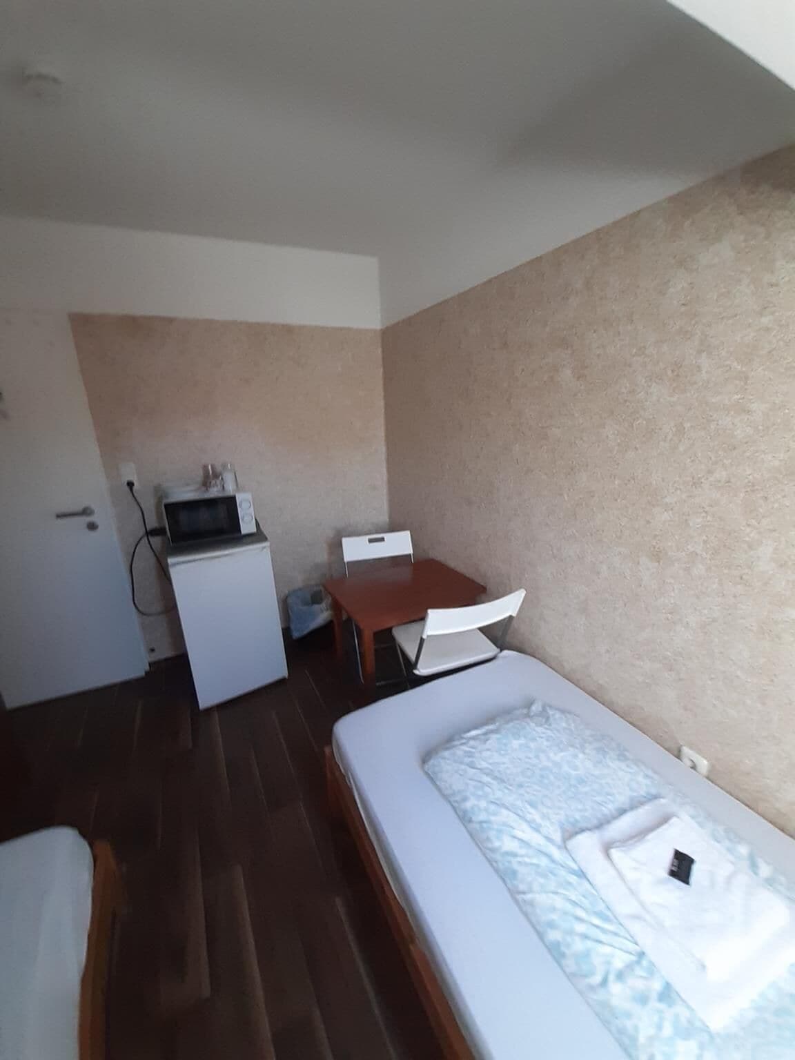 Una habitación pequeña y funcional con cama, escritorio y microondas.