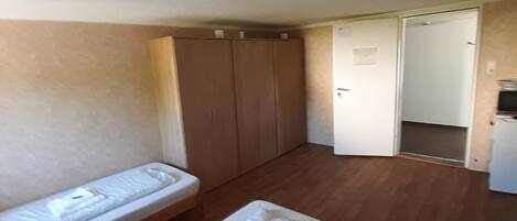 Una habitación con dos camas individuales, suelo de madera, un armario y una puerta que da a otra habitación.