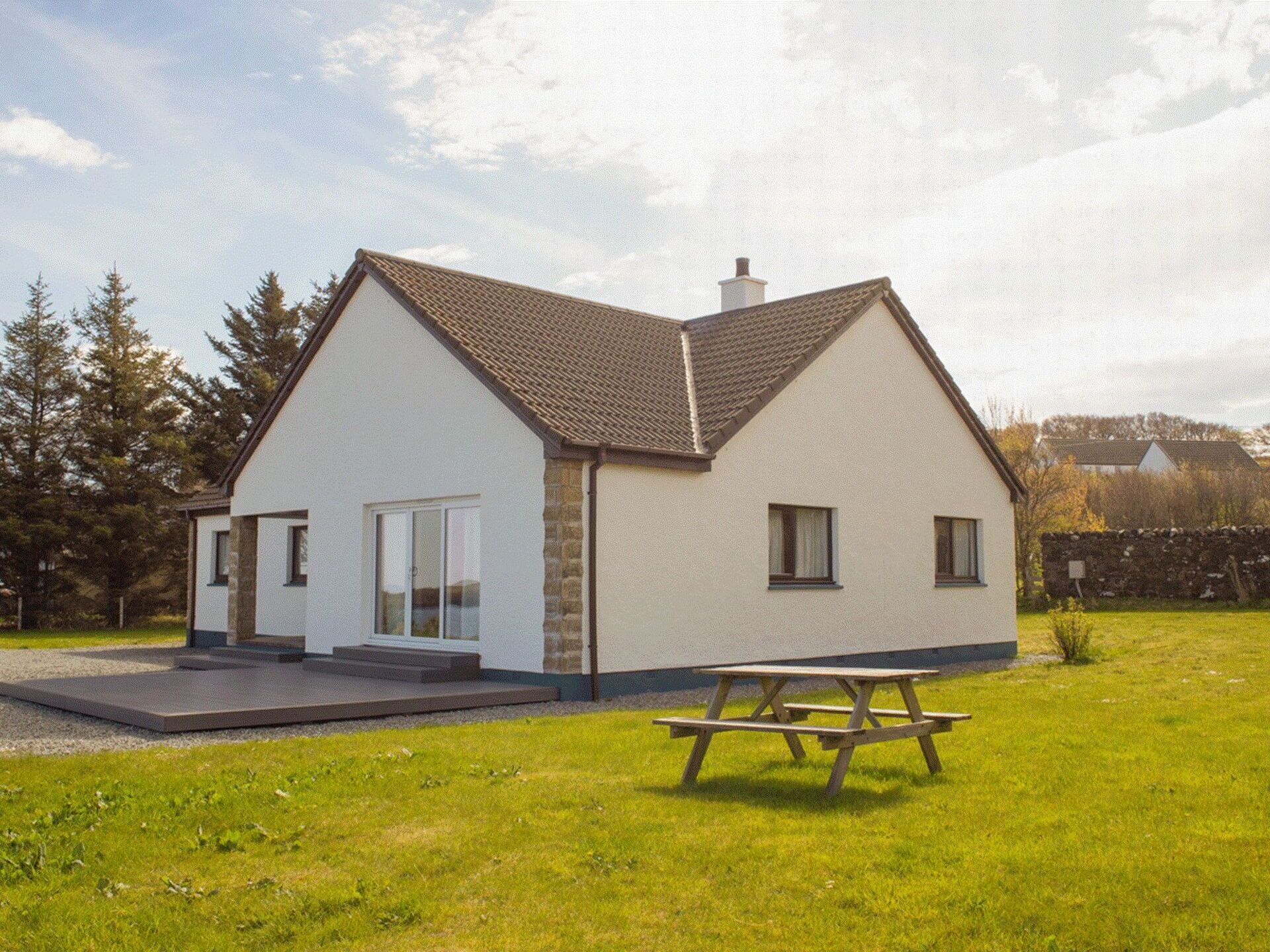 A modern two-story house with a sloped roof, a patio, and a picnic table in the front yard.